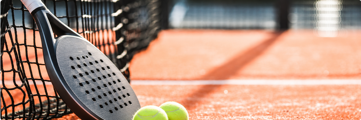 Padel racket and balls on a sunlit court, ready to serve